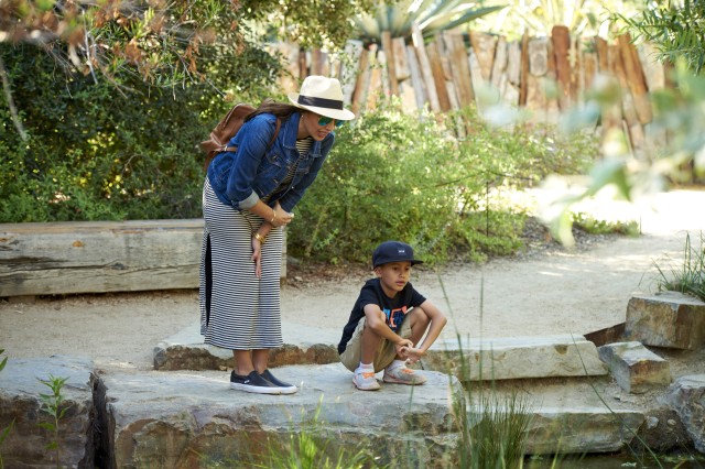 A woman in a sun hat and a boy in a baseball hat by the side of the pond