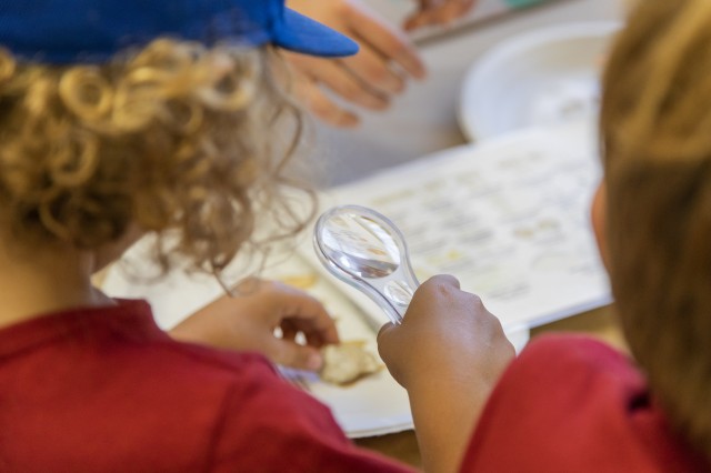 the back of two children&#039;s heads, one of them is holding a magnifying lense and a small fossil