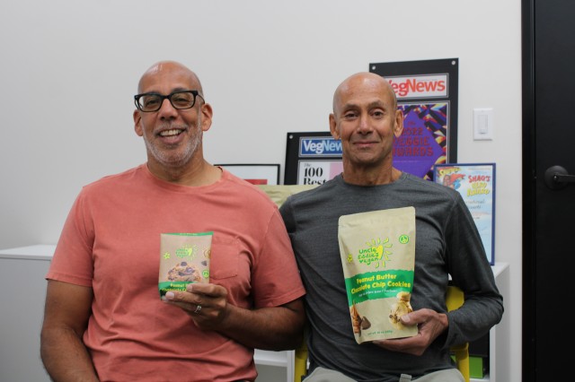two men sit holding bags of cookies 