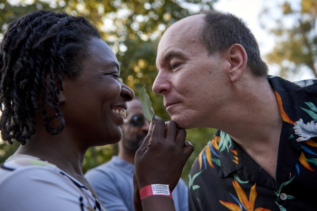 Visitor holding up a leaf to another visitor leaning in to smell the leaf