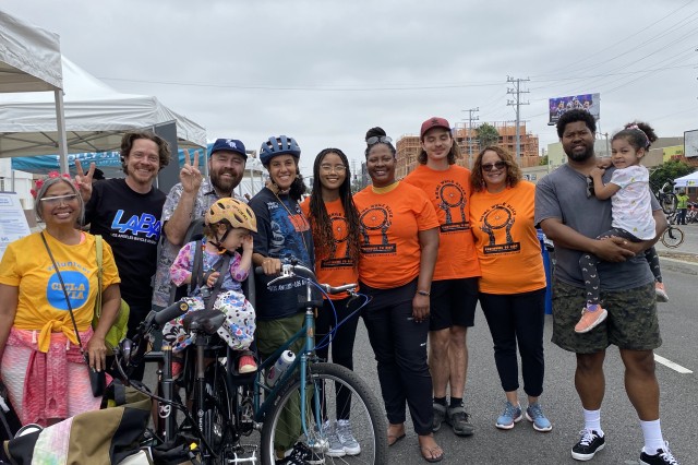 A group of BIPOC children and adults pose around two bicycles