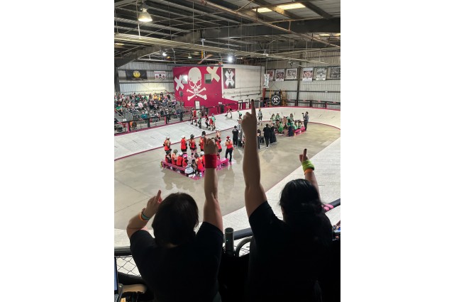 Two fans cheering in the stands as they look down at players in a banked roller derby track