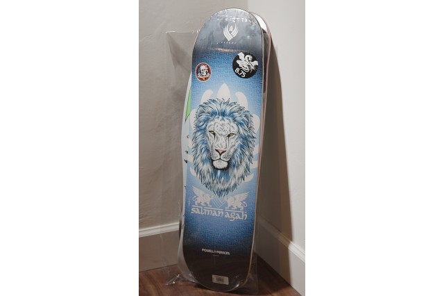 Gray, white and blue skateboard deck with the head of a lion in the center.