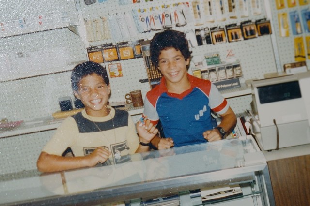 Two school-age boys, circa 1980s, smiling behind the counter of an office supply store.