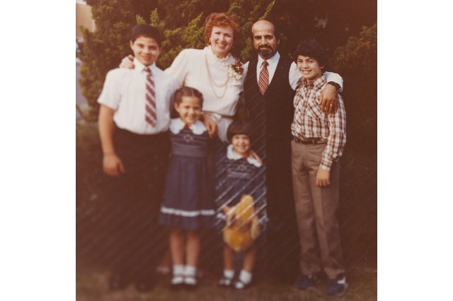1980s-style, formal family photo with parents in the middle, their two sons on either side of them, and the two young daughters in front.