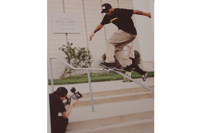 Skateboarder skating down an outdoor handrail with a videographer filming him from below.