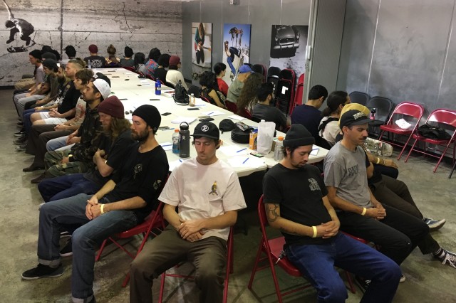 Thirty adults, men and women, sitting around a large rectangular table with their backs to the table, eyes are closed and hands are in their laps in a group medication exercise.