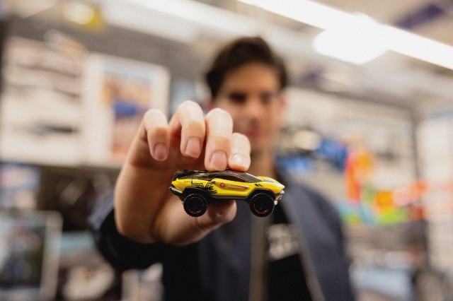 A man holds up a yellow and black Hot Wheel racecar with the number 9 and the text &#039;Angulo Racing&#039;