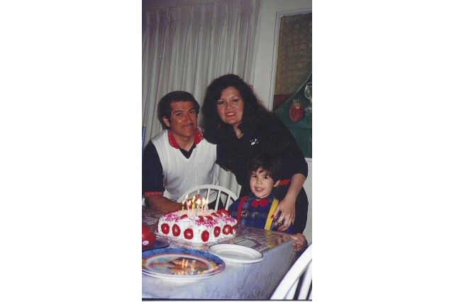 A couple and their small child stand behind a cake with lit birthday candles