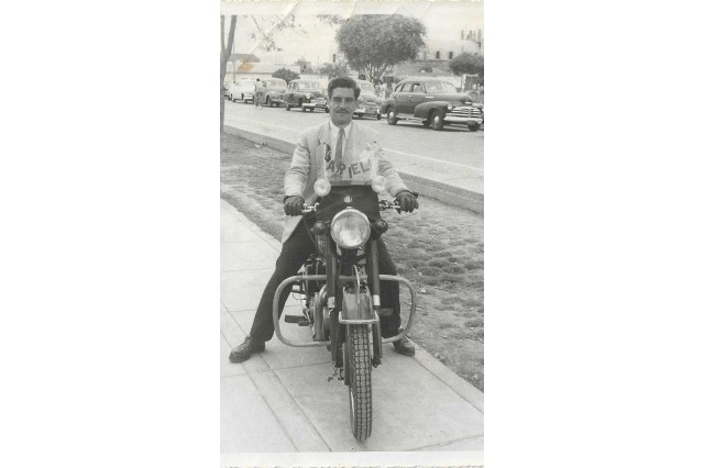 A man sits on top of a cafe racer motorcycle.