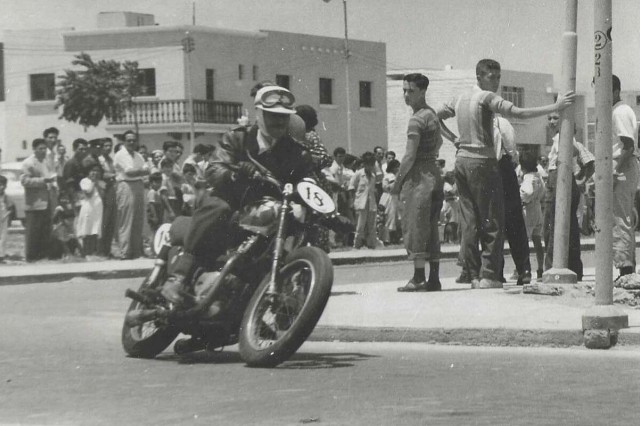 A rider on a motorcycle races around a corner while the audience watches the race.