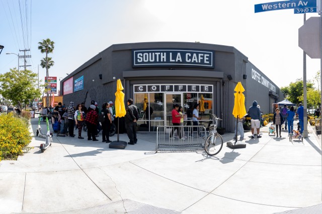 Entrance to a grey-colored corner coffee shop with a line outside the door.