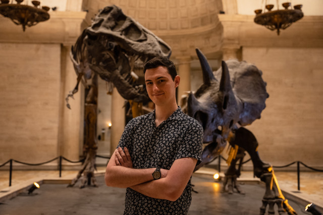 Cullen Townsend with arms across in front of two dinosaur skeletons