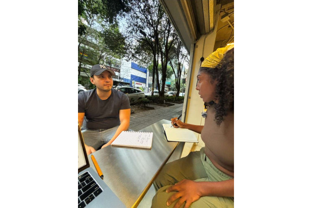 A man and woman sit at a table with notebooks and a computer.