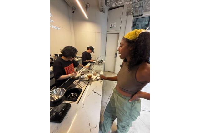 A woman waits at a minimalistic coffee shop bar while she observes the baristas across her