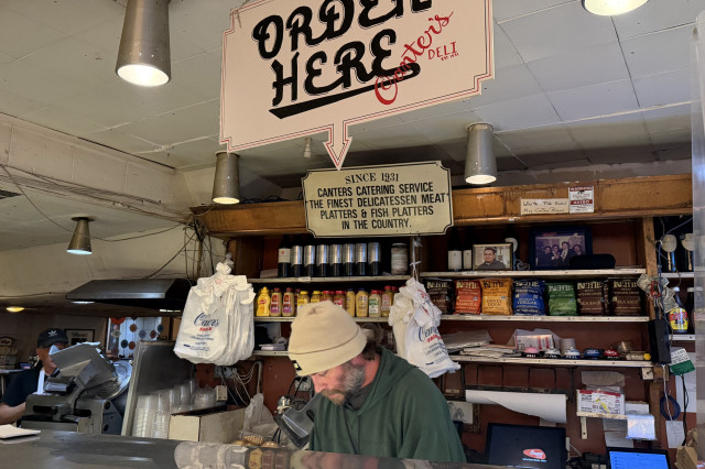Man behind a deli counter below a sign that says "Order Here".