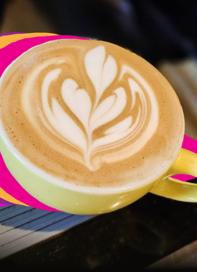 A top-down view of a latte in a yellow ceramic cup featuring heart-shaped foam art, set against a dark background with vibrant purple, pink, and orange graphic stripes flowing toward the cup.