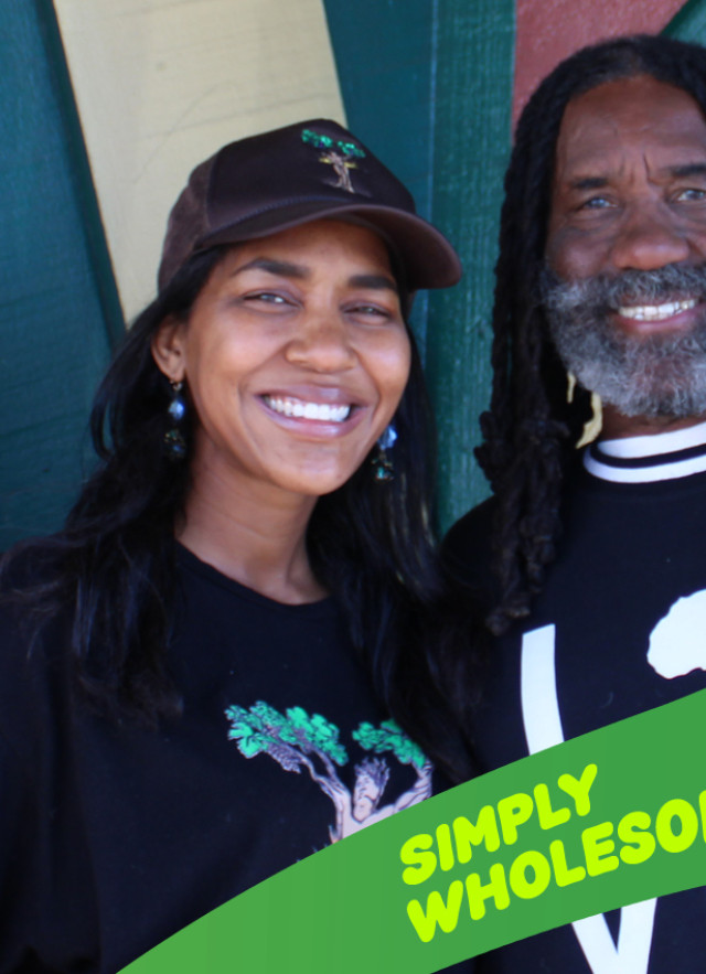 A wide, eye-level photograph shows two smiling people—a man and a woman—posed closely together inside Simply Wholesome, a restaurant and health food store in Los Angeles.