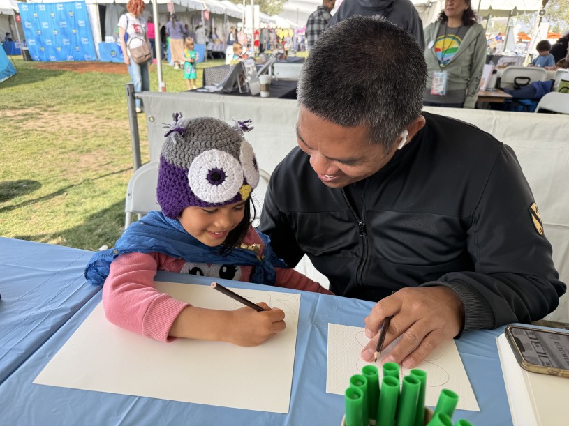 Father and daughter drawing together at an arts and crafts activity booth.