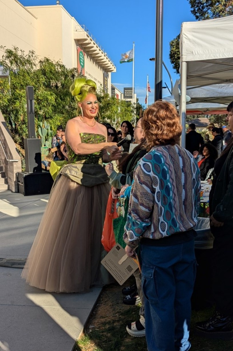 Drag queen in green wig and dress greeting guests outside in front of a museum.